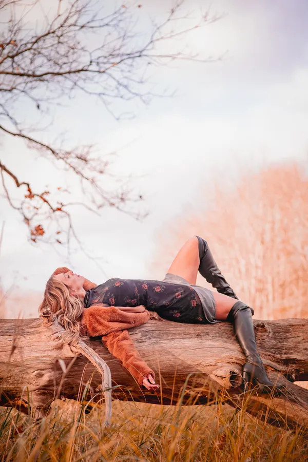 Woman in a rust coat reclining on a fallen log
