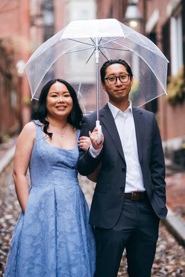 Engaged couple sharing a clear umbrella on a cobblestone street