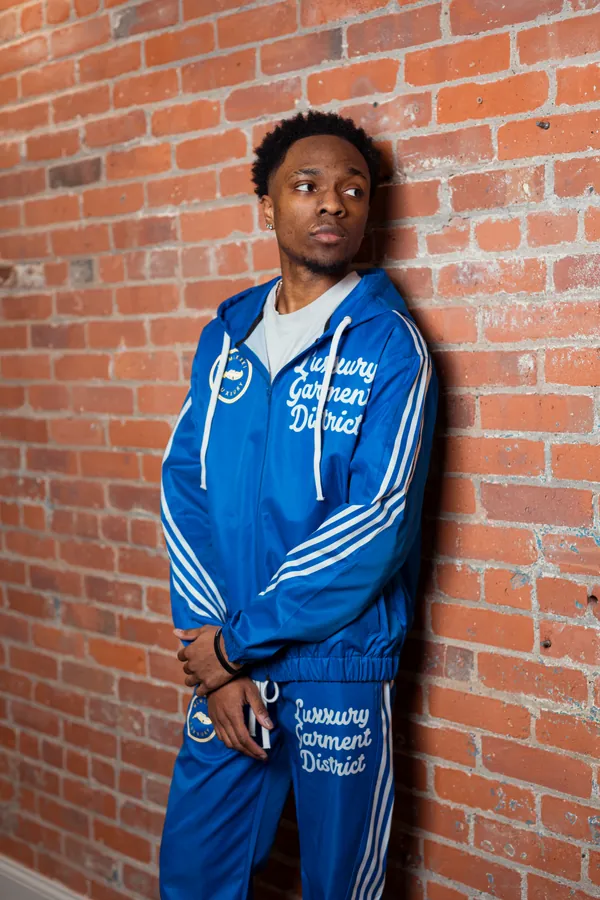 Model in a blue tracksuit leaning on a brick wall