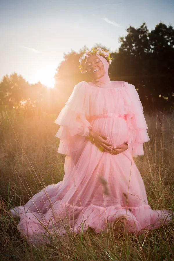 Expecting mother in a flowing pink gown in a sunlit field