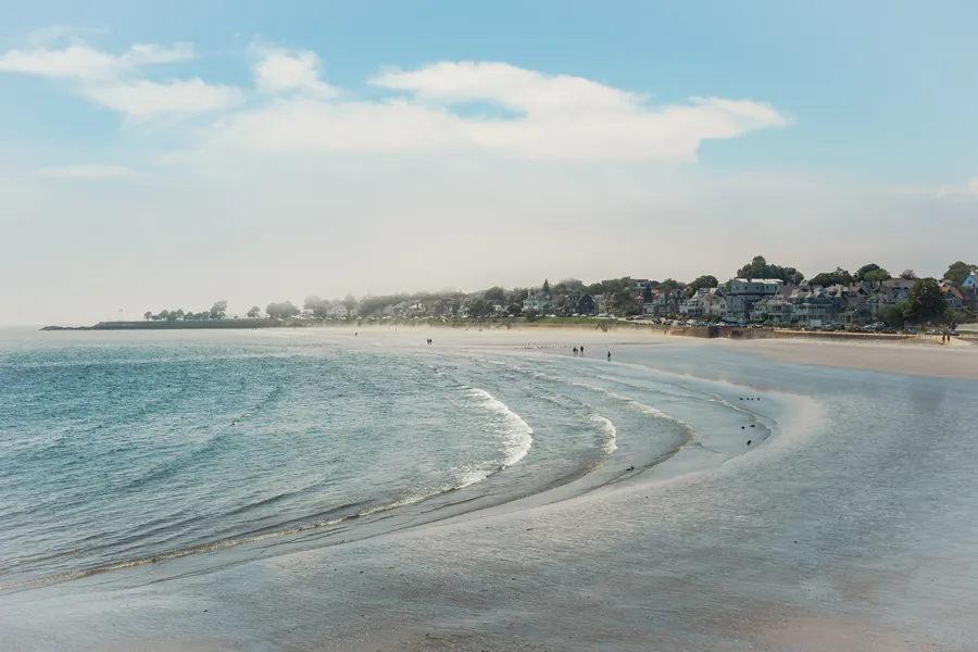 Waves curving along a New England beach under a bright sky