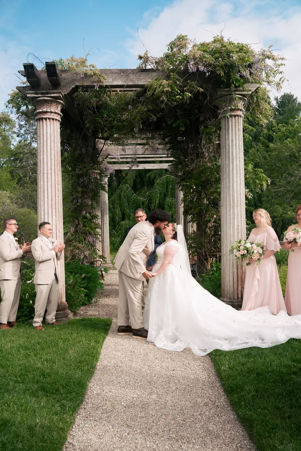 Bride and groom walking beneath a vine-covered stone pergola